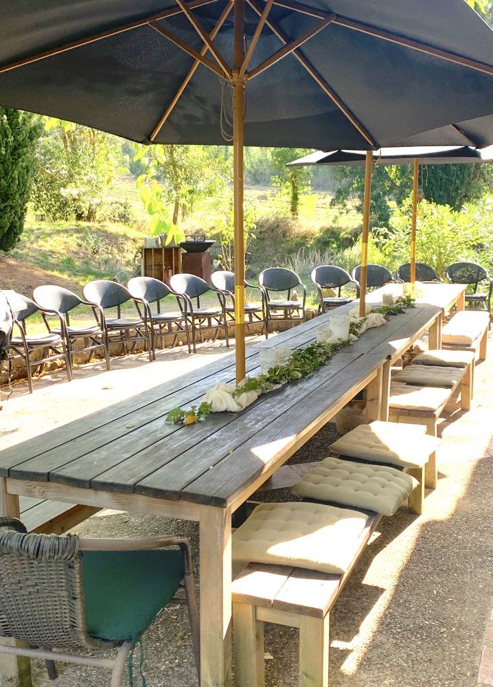 La terrasse : grande table en bois sous les parasols, face aux champs